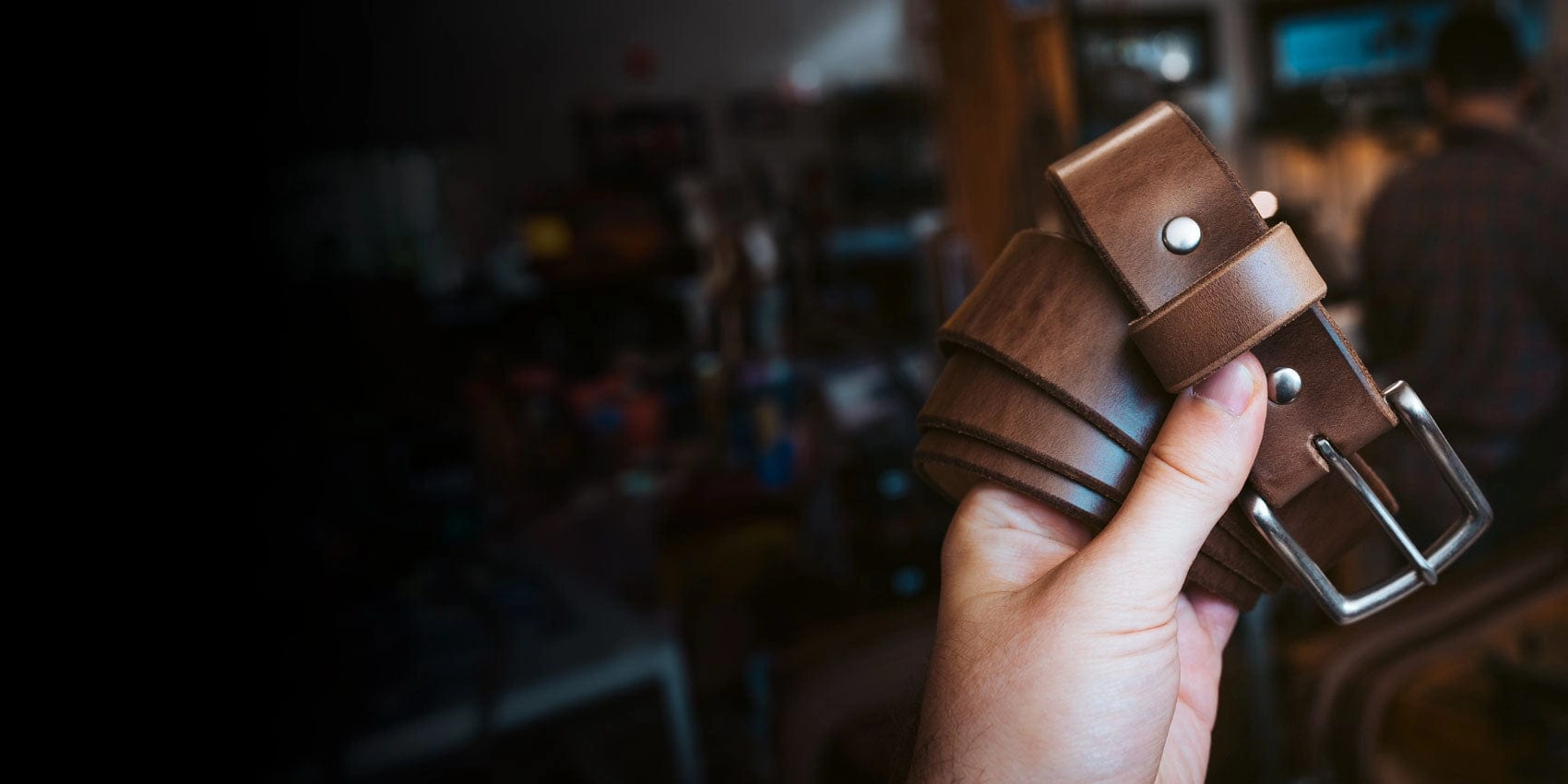 A hand holding a coiled brown leather belt with a steel buckle in the workshop