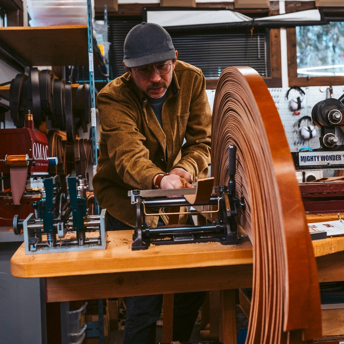 A maker cutting belt straps on a machine in the Popov Leather workshop
