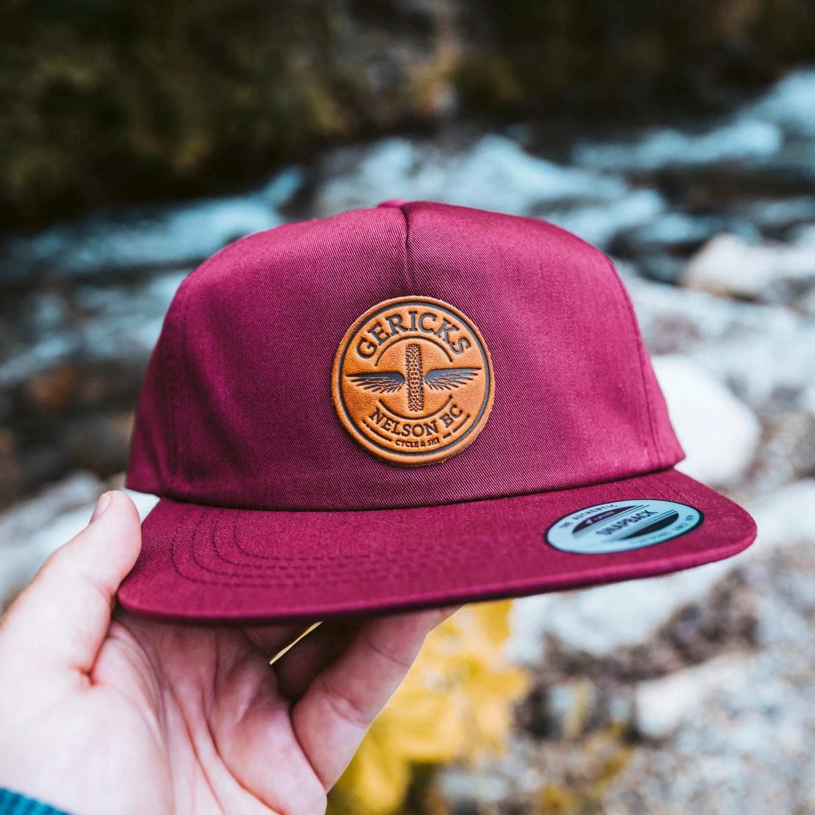 A red cap with a round stamped leather patch held over a creek