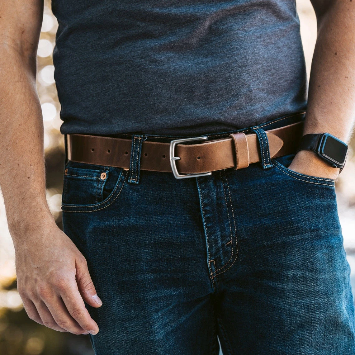 A worn brown leather belt on dark jeans