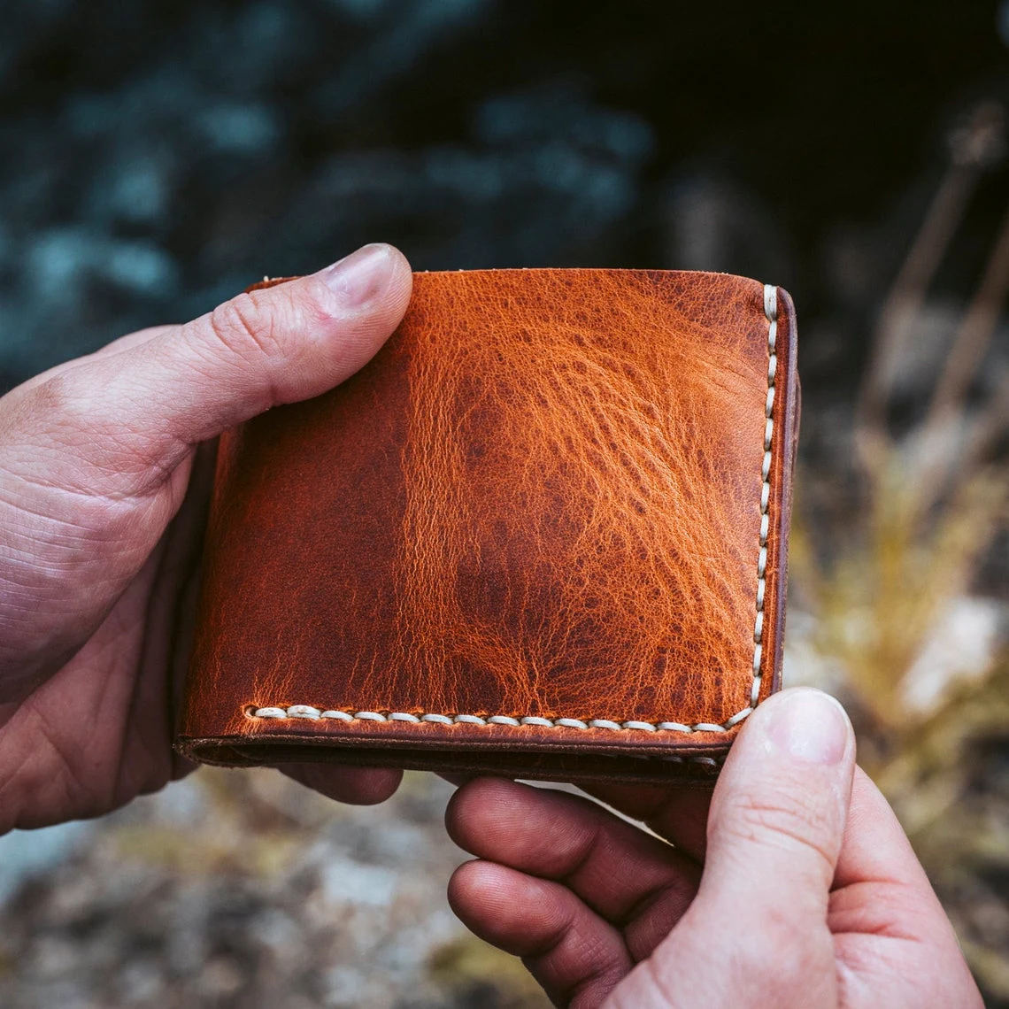 Hands holding a bifold wallet with a year of wear
