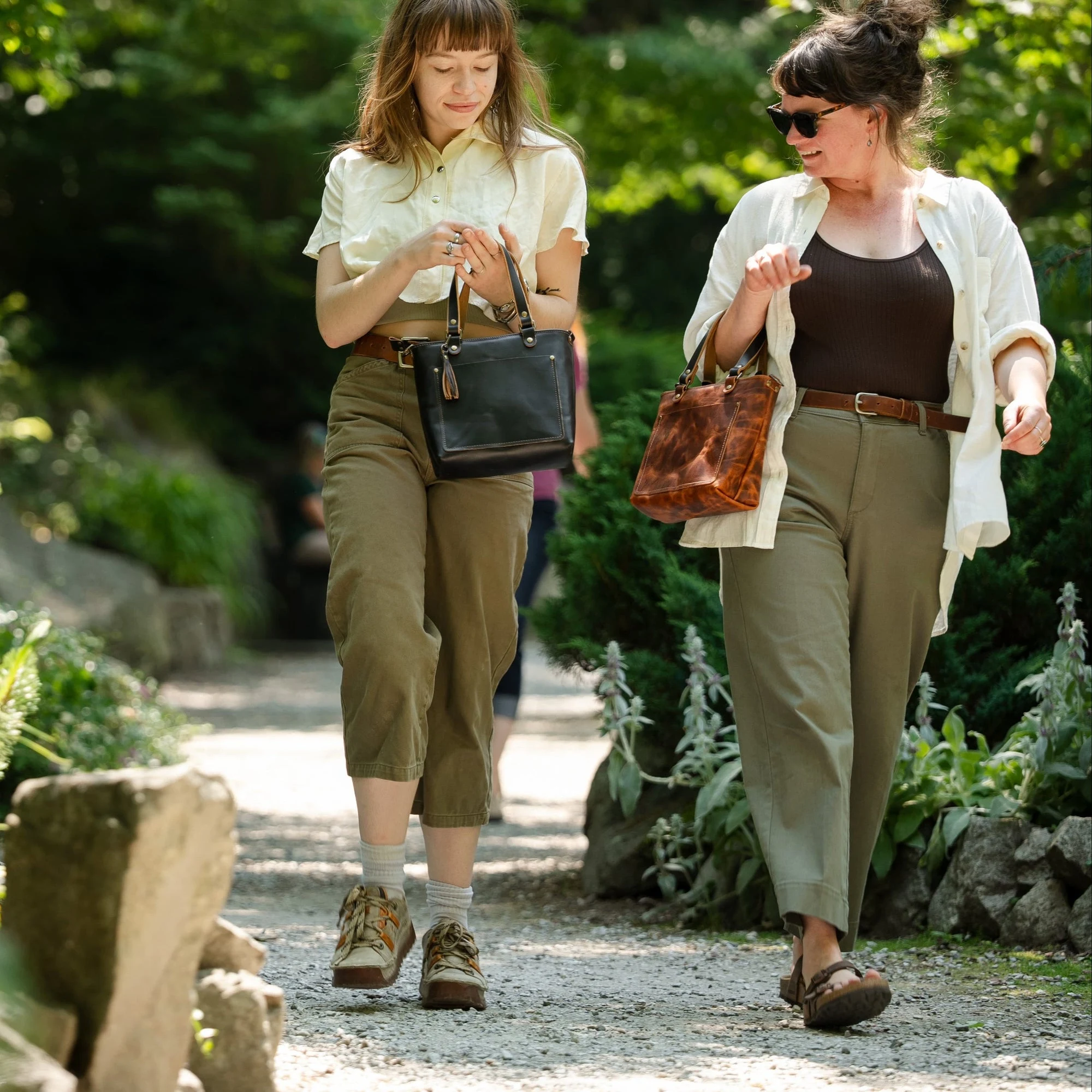 Two customers walking a garden path carrying Popov Leather bags